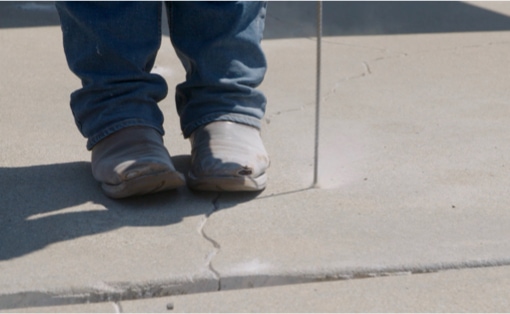 Masonry drillbit boring a hole into concrete driveway in preparation for leveling